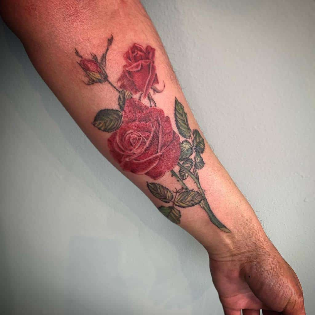 Realistic forearm tattoo of blooming red roses with detailed green leaves and stems, creating a classic and timeless floral design.