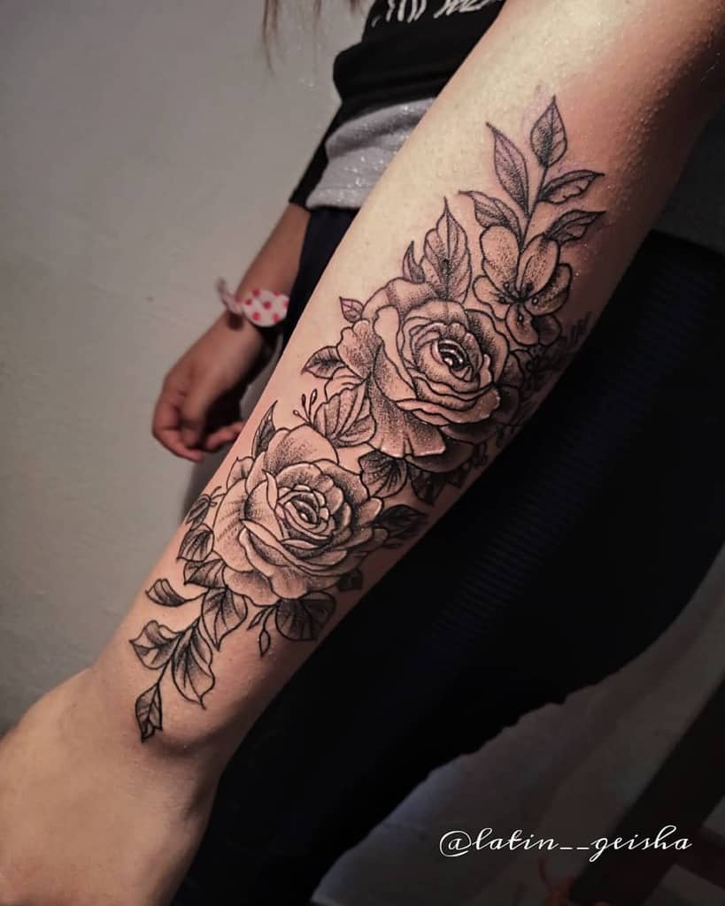 Black and grey forearm tattoo showcasing two detailed roses with intricate leaves and floral accents, combining elegance and boldness
