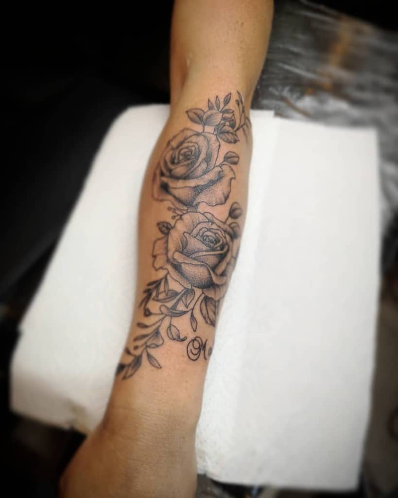 Black and grey forearm tattoo with two detailed roses, accented by delicate leafy vines for a classic and timeless floral design