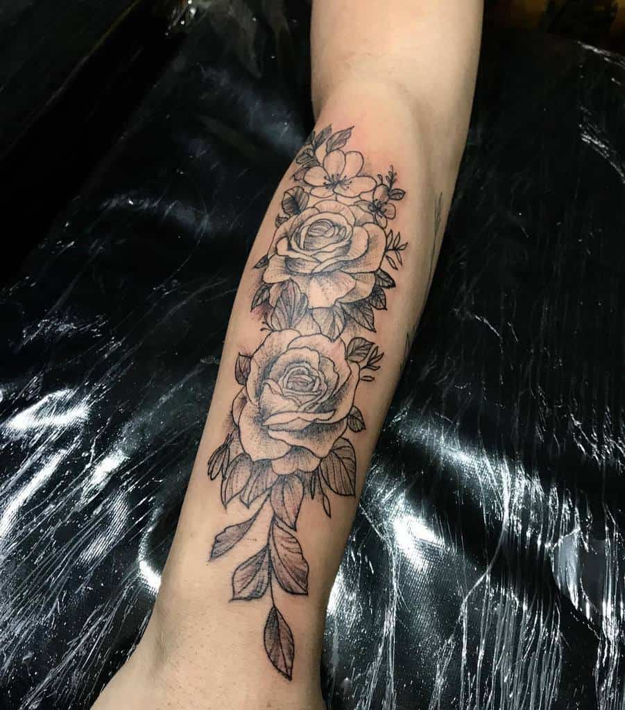 Elegant forearm tattoo featuring two roses and delicate blossoms, accented by detailed leaves for a graceful and timeless design