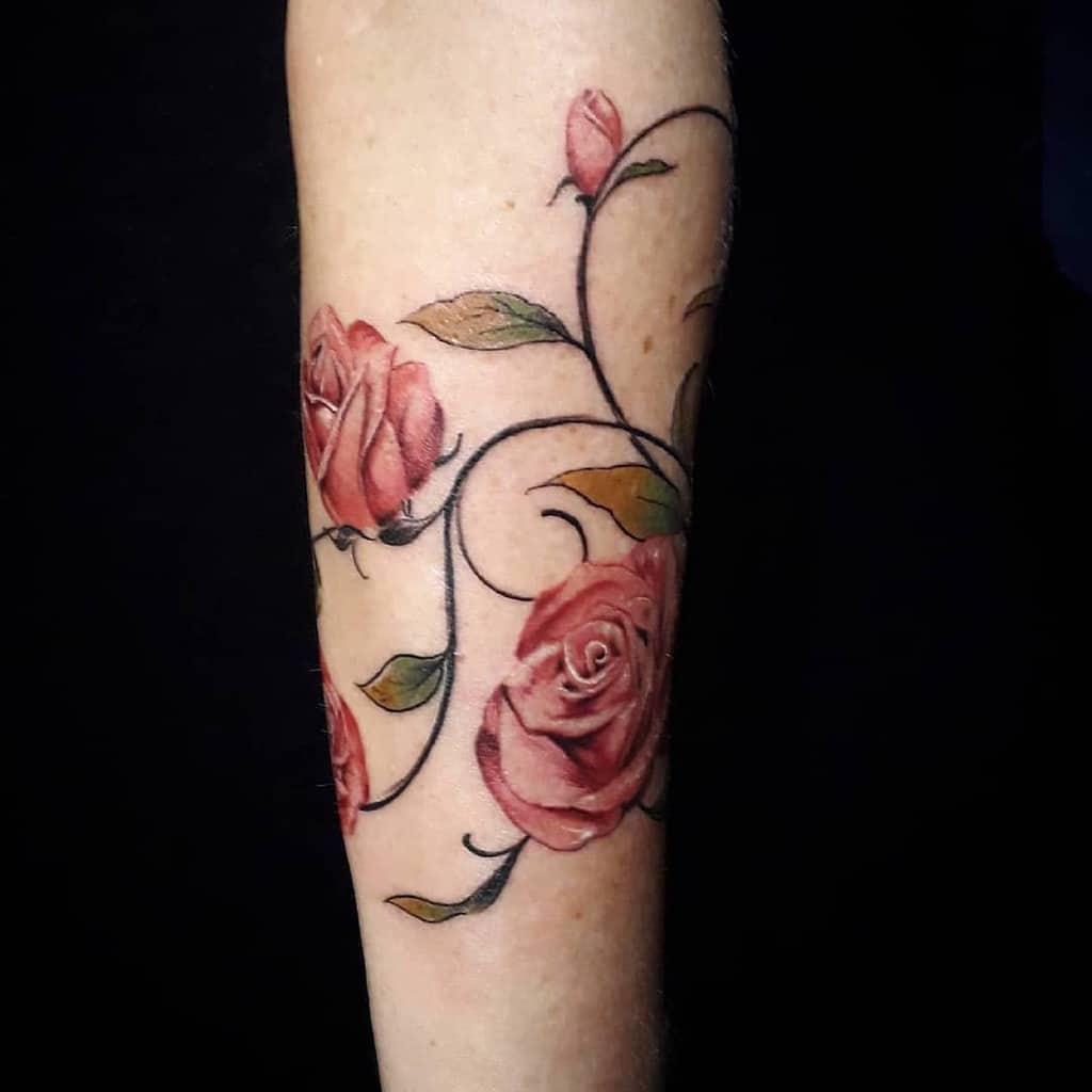 Forearm tattoo featuring vibrant pink roses with elegant swirling vines and soft green leaves, creating a graceful floral composition