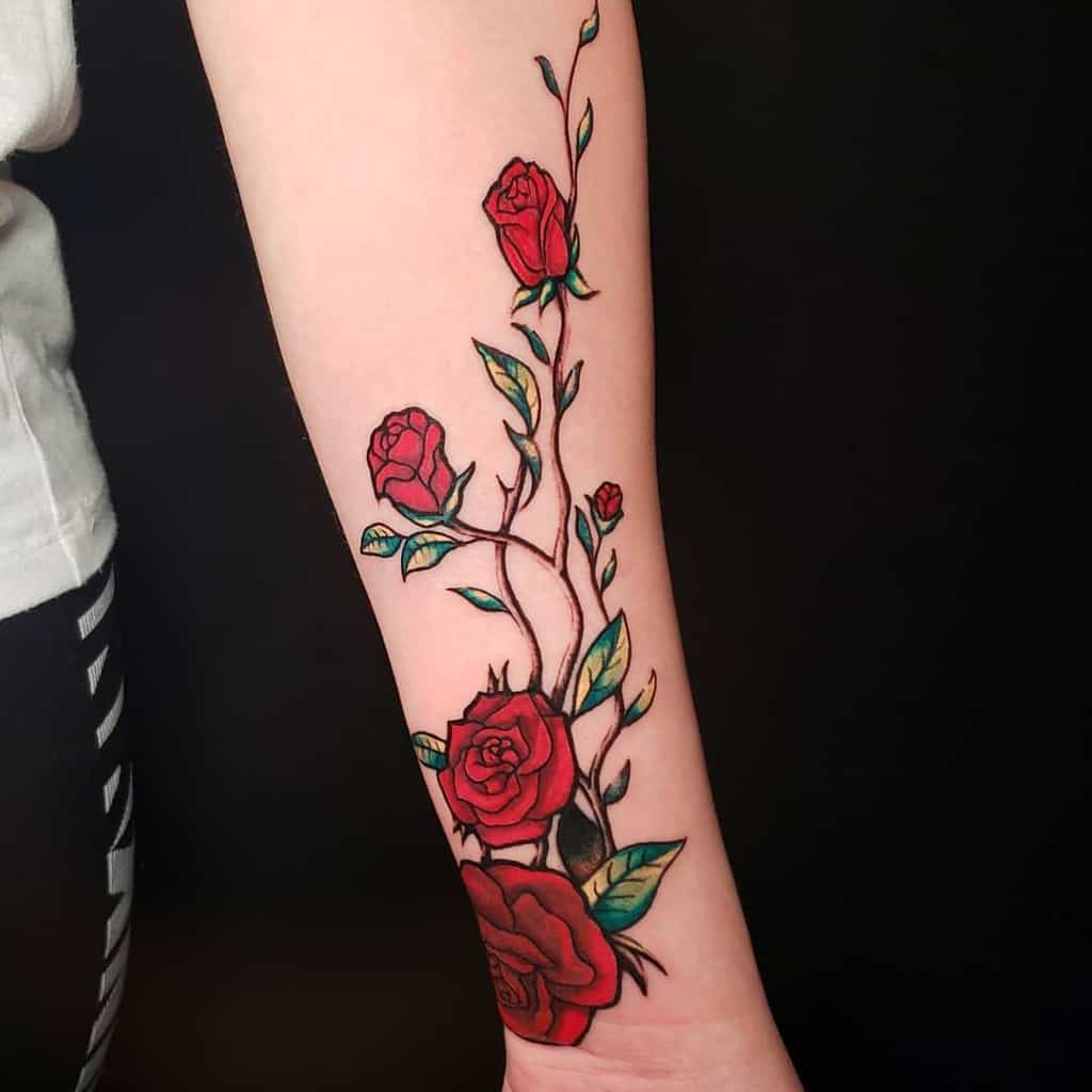 Forearm tattoo with vivid red roses and intertwining vines, highlighted by vibrant green leaves for a bold and striking floral design
