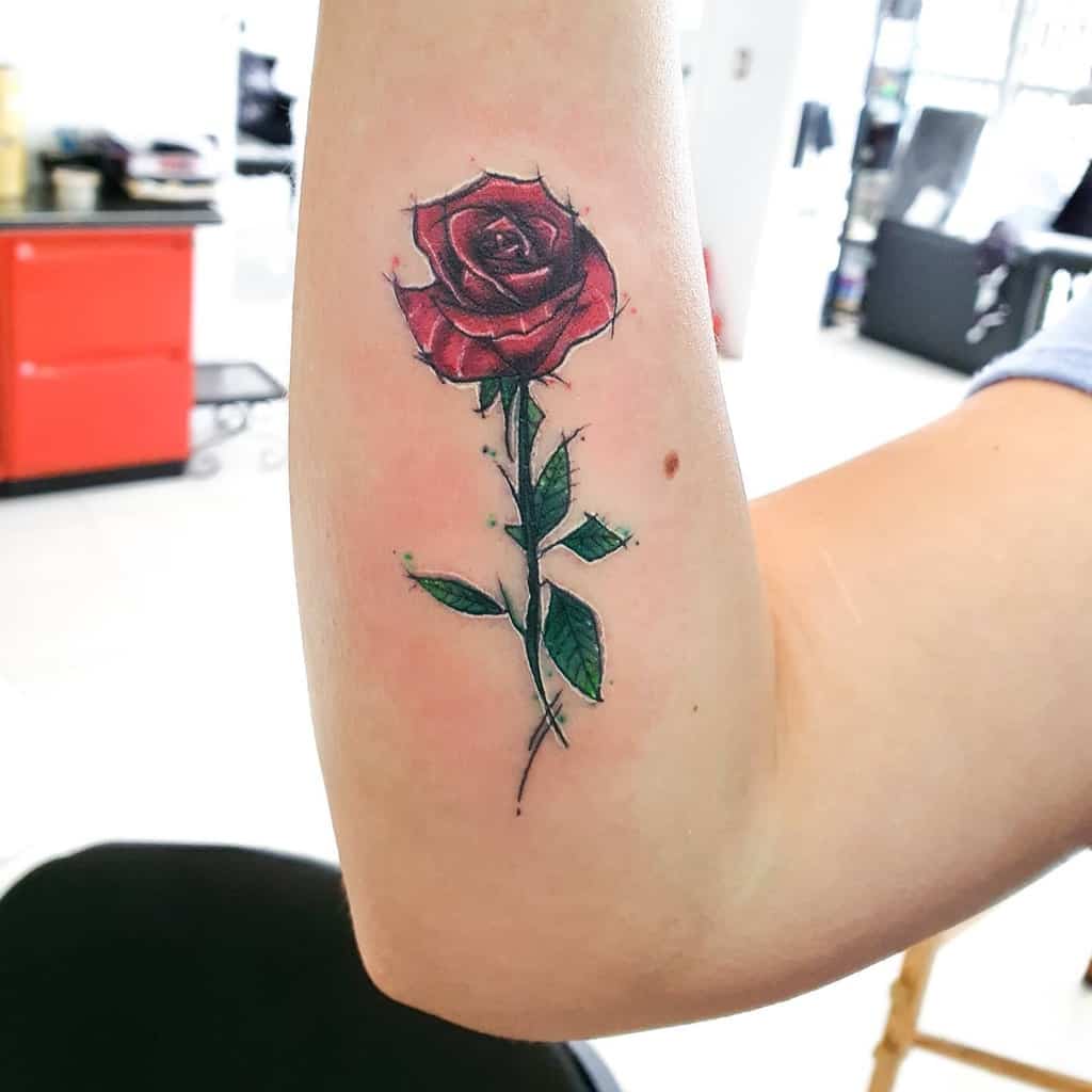 A red rose tattoo with lush green leaves and a delicate stem sneaks up the arm