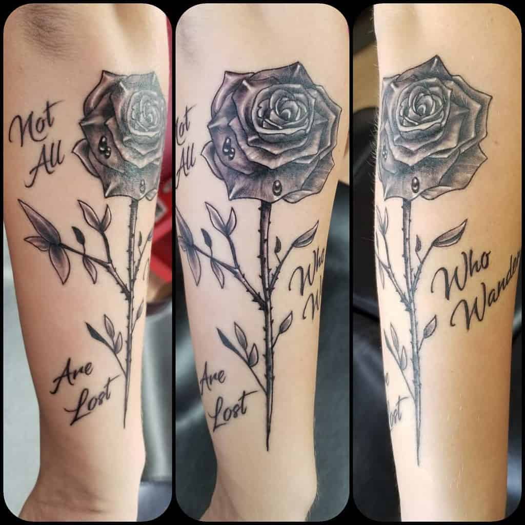 Rose tattoo with a delicate stem and the text: "Not all who wander are lost" elegantly inked on an arm
