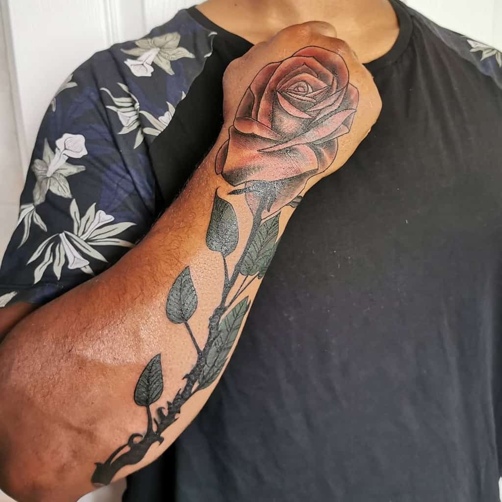 A forearm tattoo of a large rose, intricately detailed with a long stem and lush leaves