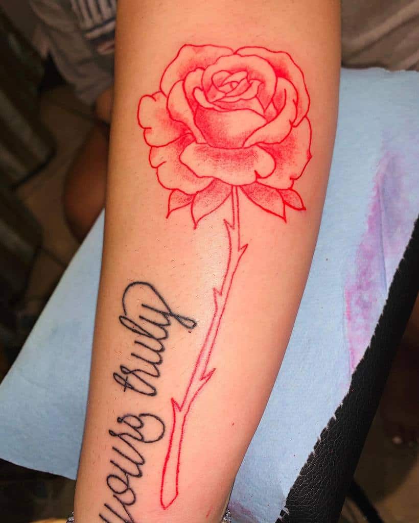 A red rose tattoo, complete with a delicate stem, graces the forearm alongside the words "yours truly"