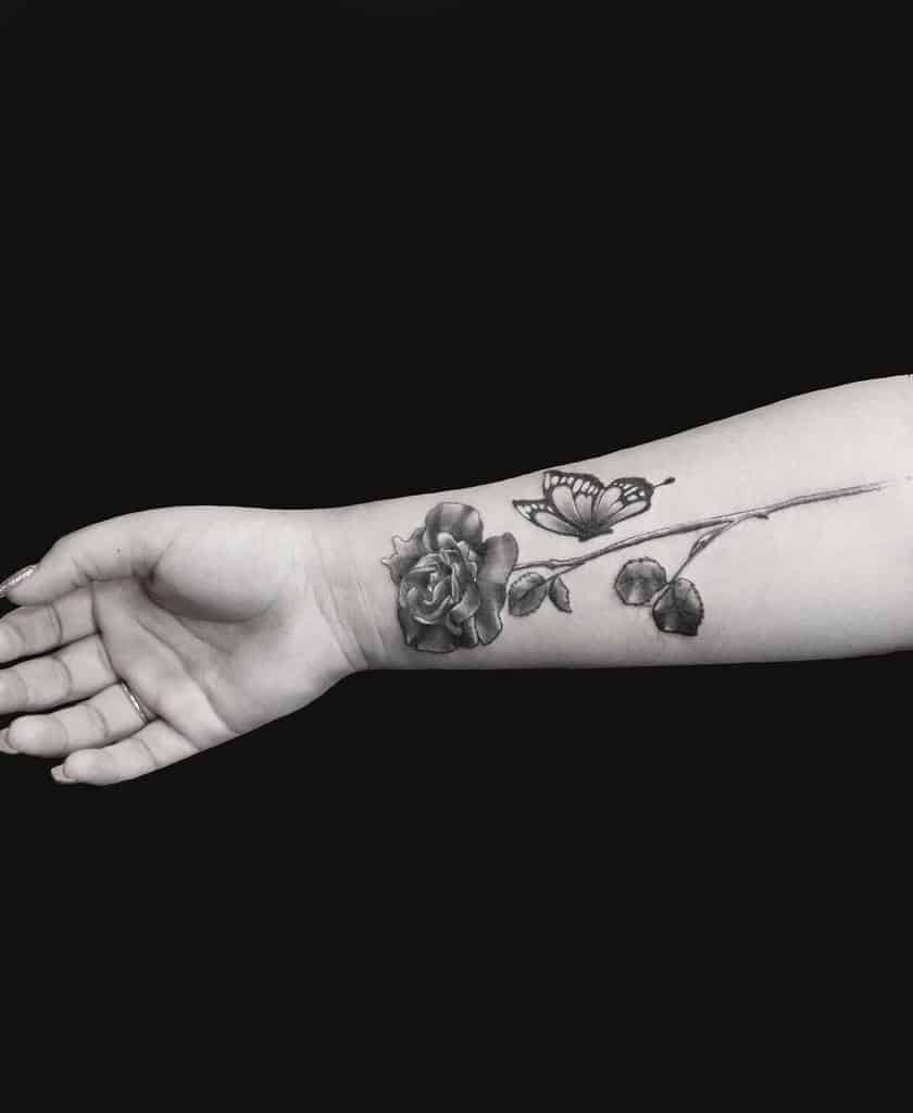 Tattoo of a rose with an elegant stem and a butterfly on a person's forearm