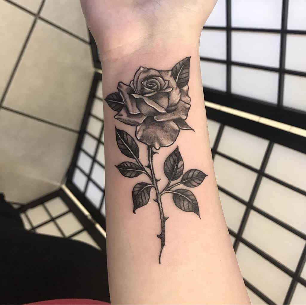 A black rose tattoo with an intricate stem elegantly winds down the forearm