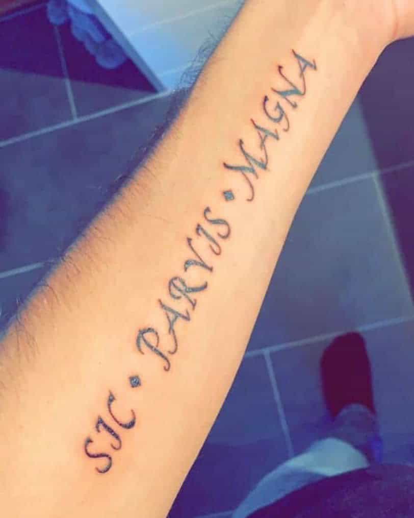 Tattoo on forearm reading "Sic Parvis Magna" in dark ink