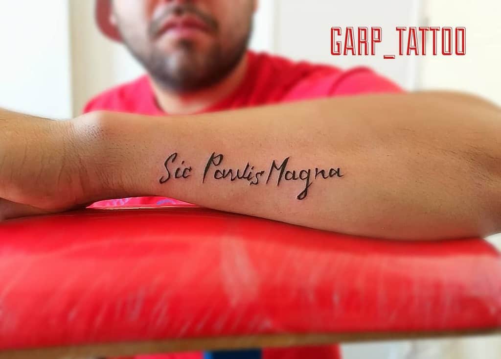 Person with a forearm tattoo reading "Sic Parvis Magna" in script font