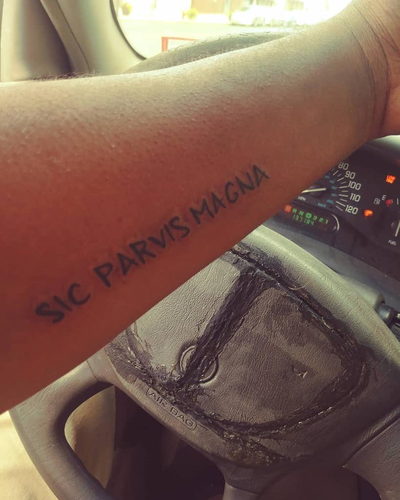 Forearm tattoo with "SIC PARVIS MAGNA" while holding a steering wheel