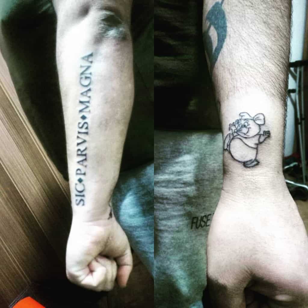Side-by-side tattoos on forearm and wrist: text "Sic Parvis Magna" and a cartoon bear