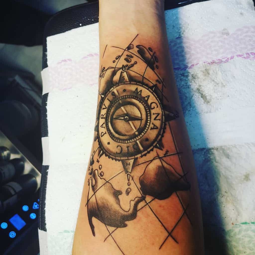 Forearm tattoo of a compass and world map with the phrase "Sic Parvis Magna" on a compass design