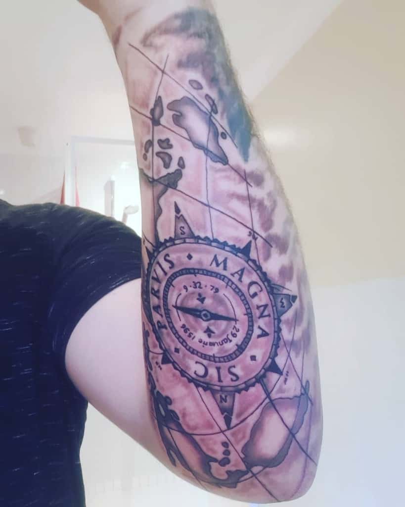 Inner forearm tattoo of a compass with 'Sic Parvis Magna' text overlaid on a detailed world map design