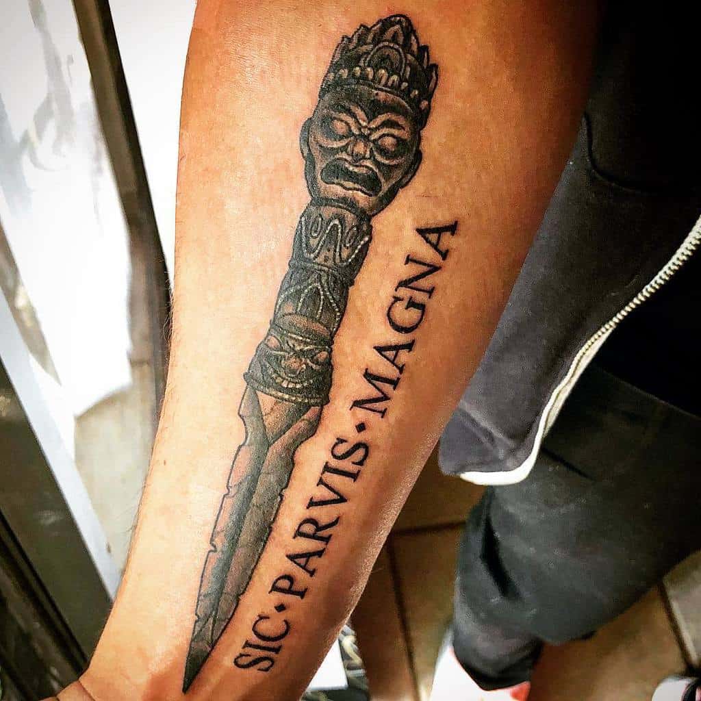 Arm tattoo of a dagger with a wooden hilt, featuring the phrase "Sic Parvis Magna"