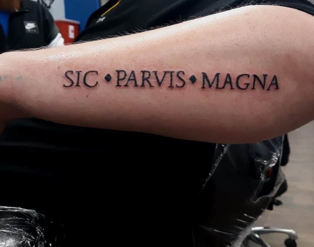 Forearm tattoo with the phrase "SIC • PARVIS • MAGNA" in black ink