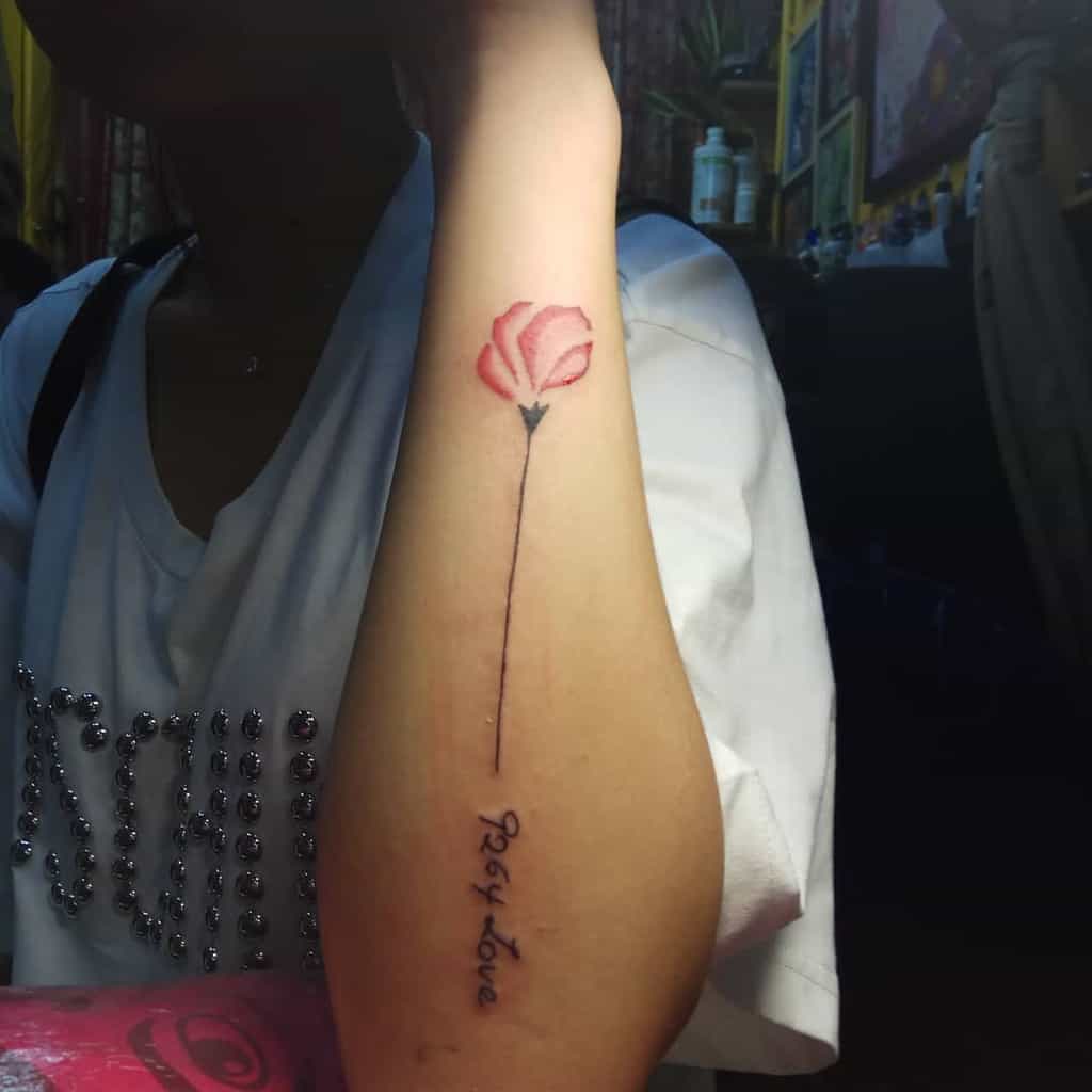Forearm features a rose tattoo with a stem forming the words "self love" in a cursive script