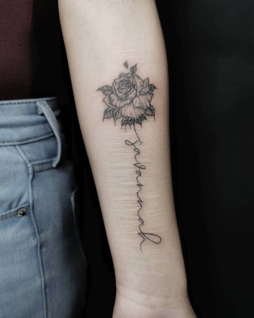 Tattoo of a rose with cursive text below it on a forearm