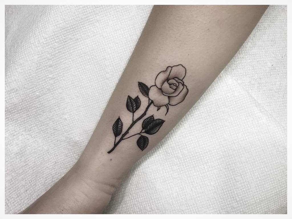 Black and grey rose tattoo with leaves on a forearm