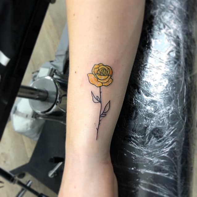 Tattoo of a minimalistic yellow rose with a long stem on a forearm