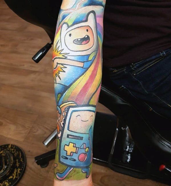 Colorful Adventure Time tattoo sleeve featuring Finn, BMO, and a rainbow background on a man's forearm.