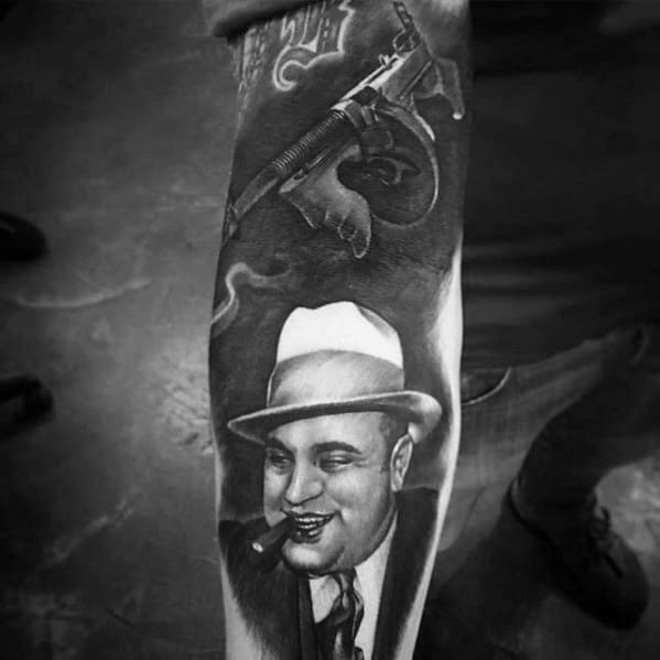 Al Capone tattoo featuring a black-and-white portrait of the gangster smiling with a cigar, accompanied by a vintage Tommy gun in the design.