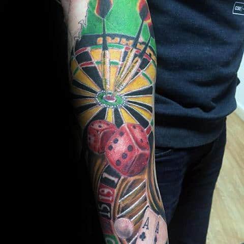 Vibrant sleeve tattoo featuring a dartboard, darts, red dice, roulette wheel, and playing cards, blending themes of skill and chance.