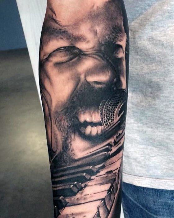 Hyper-realistic forearm tattoo of James Hetfield screaming into a mic, with guitar fretboard details extending down the arm.