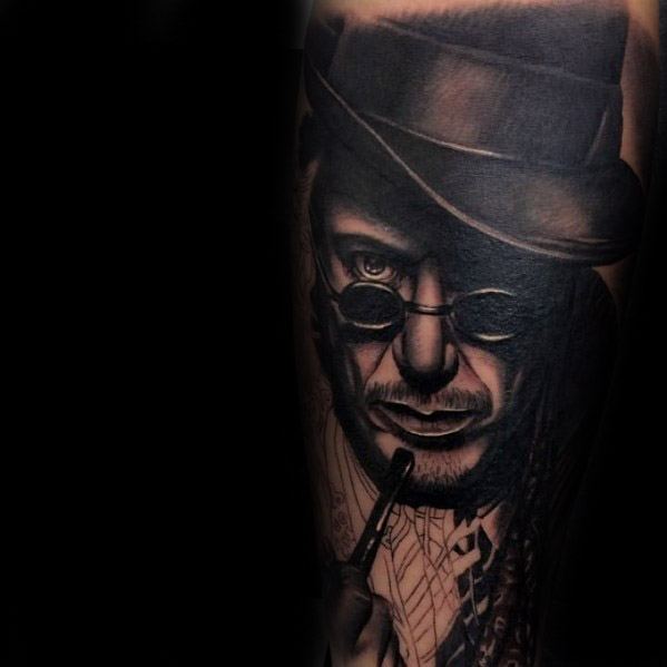 Tattoo of a man resembling Sherlock Holmes in a bowler hat with round glasses and a pipe against a dark background