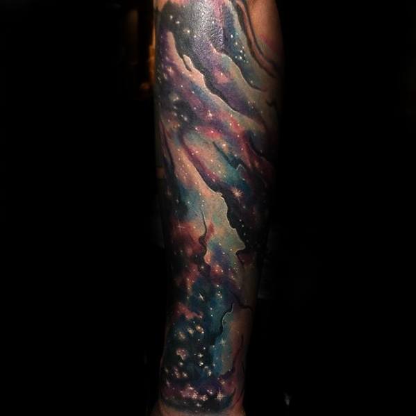 A forearm nebula tattoo with a colorful galaxy, swirling stars, and vibrant nebulae on a dark background