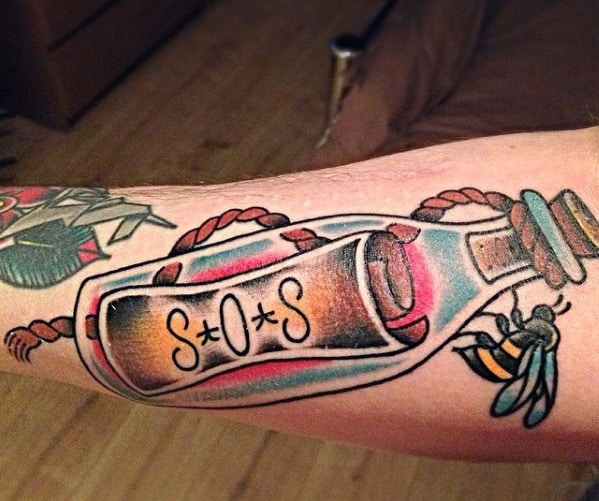 Tattoo of an SOS message in a bottle with a bee buzzing on an arm