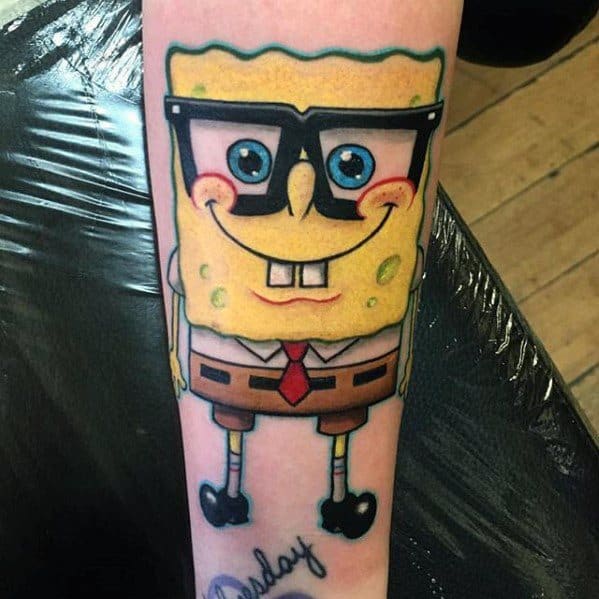 Colorful SpongeBob tattoo on forearm featuring him with nerdy glasses, bright smile, and classic outfit.