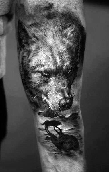Black and white tattoo of a wolf and a small silhouette of a wolf on an arm