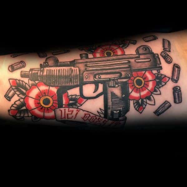 Uzi tattoo with red flowers, bullet casings, and a banner reading 'Uzi Posse.' Bold black outlines and vibrant shading on the arm.