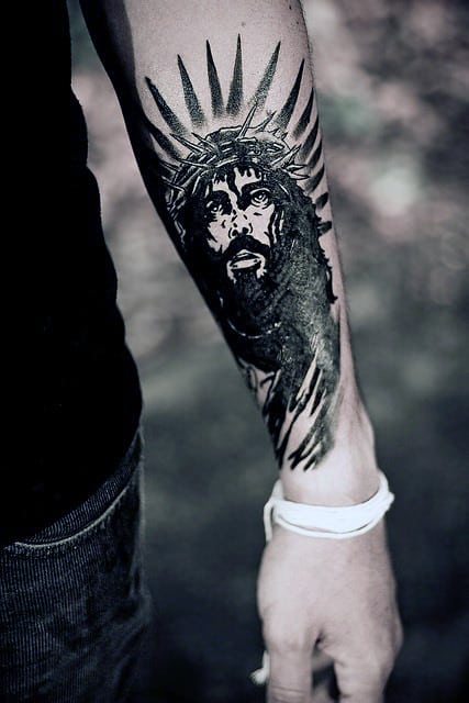 Forearm tattoo depicts the face of Jesus with a crown of thorns and radiant beams