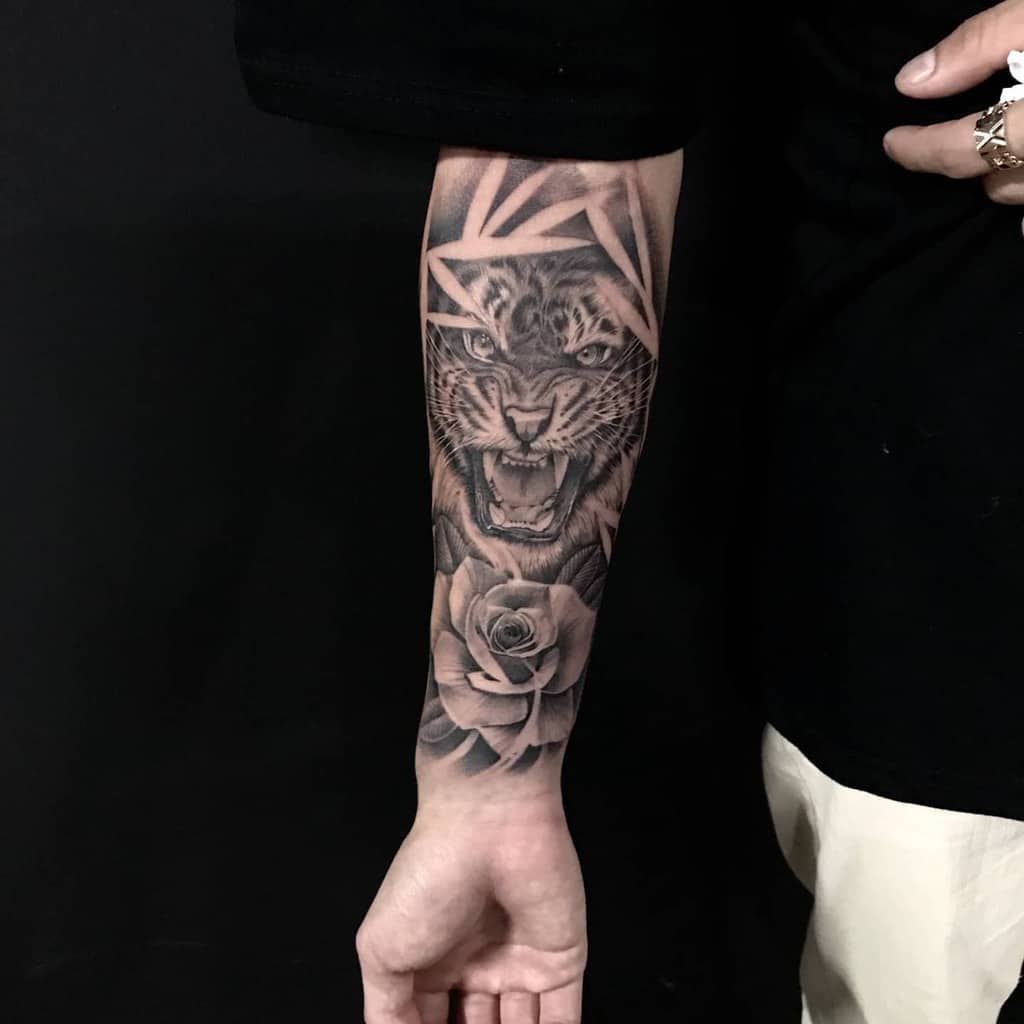 A forearm tattoo featuring a ferocious tiger's face, intertwined with geometric lines and accentuated by a rose beneath it