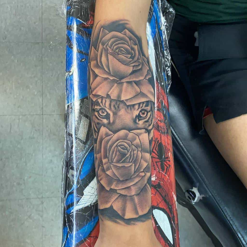 Forearm tattoo showcasing a fierce tiger's face nestled between two intricately detailed roses