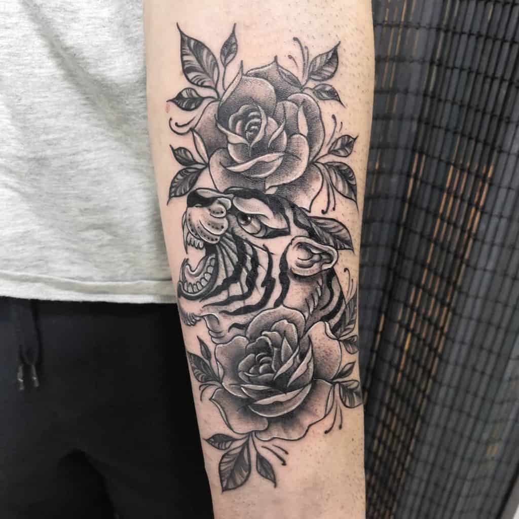 Forearm tattoo of a majestic tiger, its roar echoing through intricately detailed roses and leaves, all crafted in striking black ink