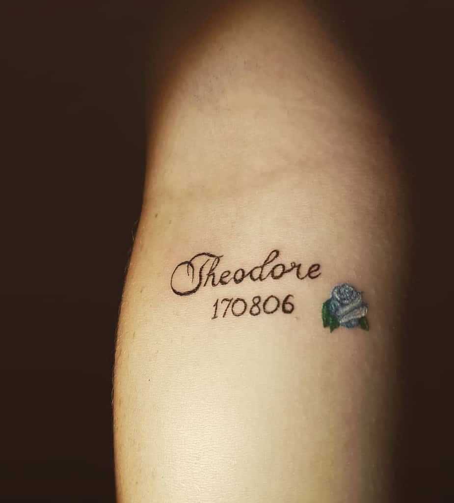 Tattoo with the name "Theodore," the number "170806," and a small blue rose on skin