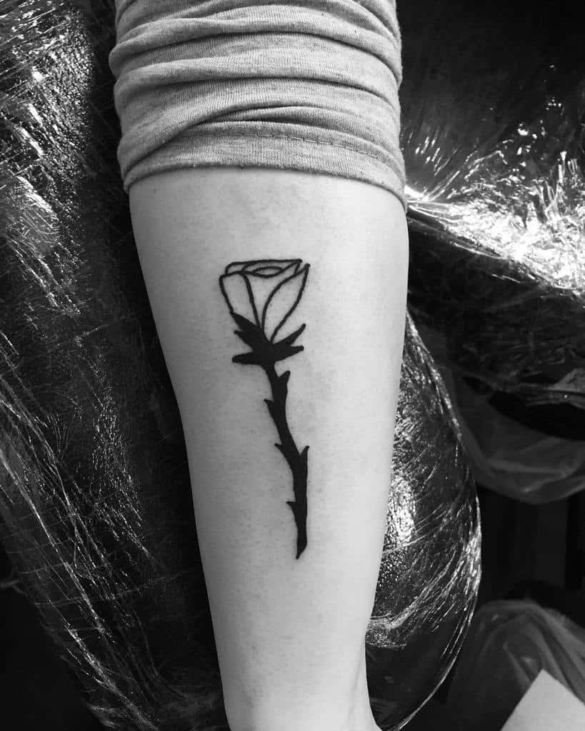 A black rose tattoo on the forearm showcases a simple, clean design, subtly incorporating tribal elements for an edgy twist