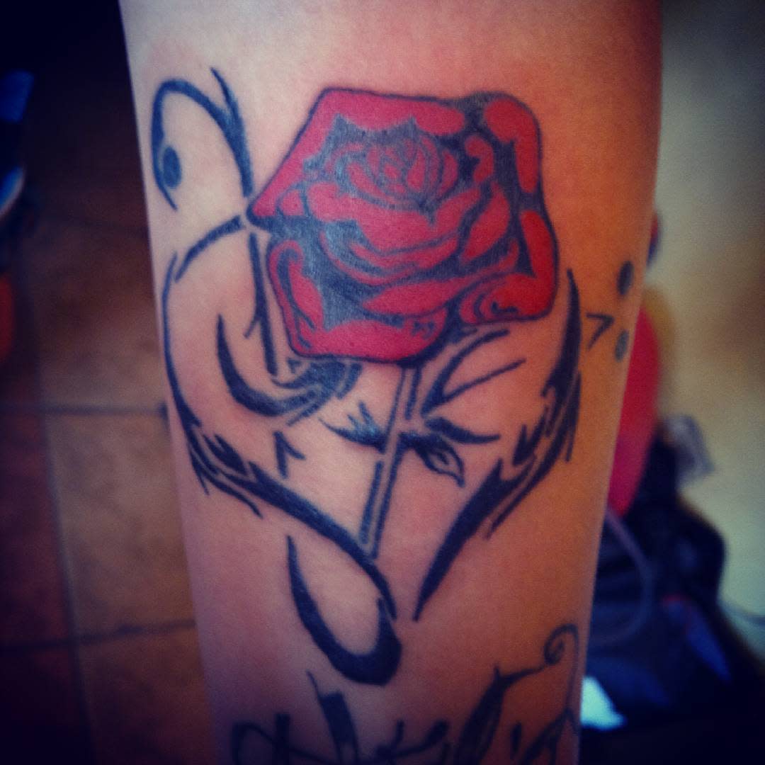 Arm tattoo of a vibrant red rose intertwined with tribal black decorative swirls