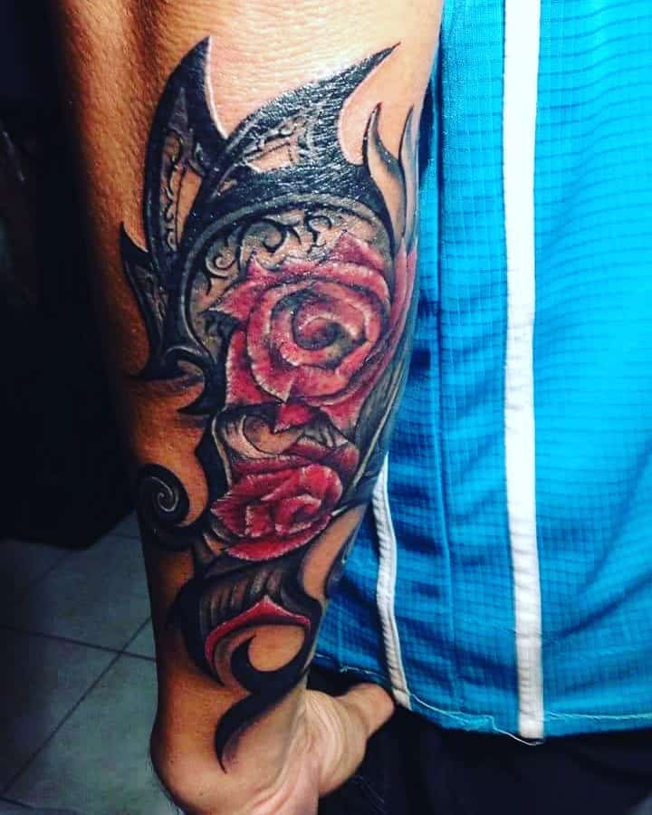 Arm tattoo featuring a vibrant rose nestled within a striking black tribal design