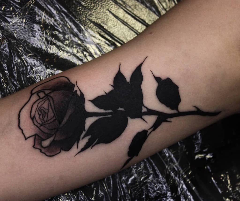 Arm tattoo of a tribal rose with dark leaves and petals