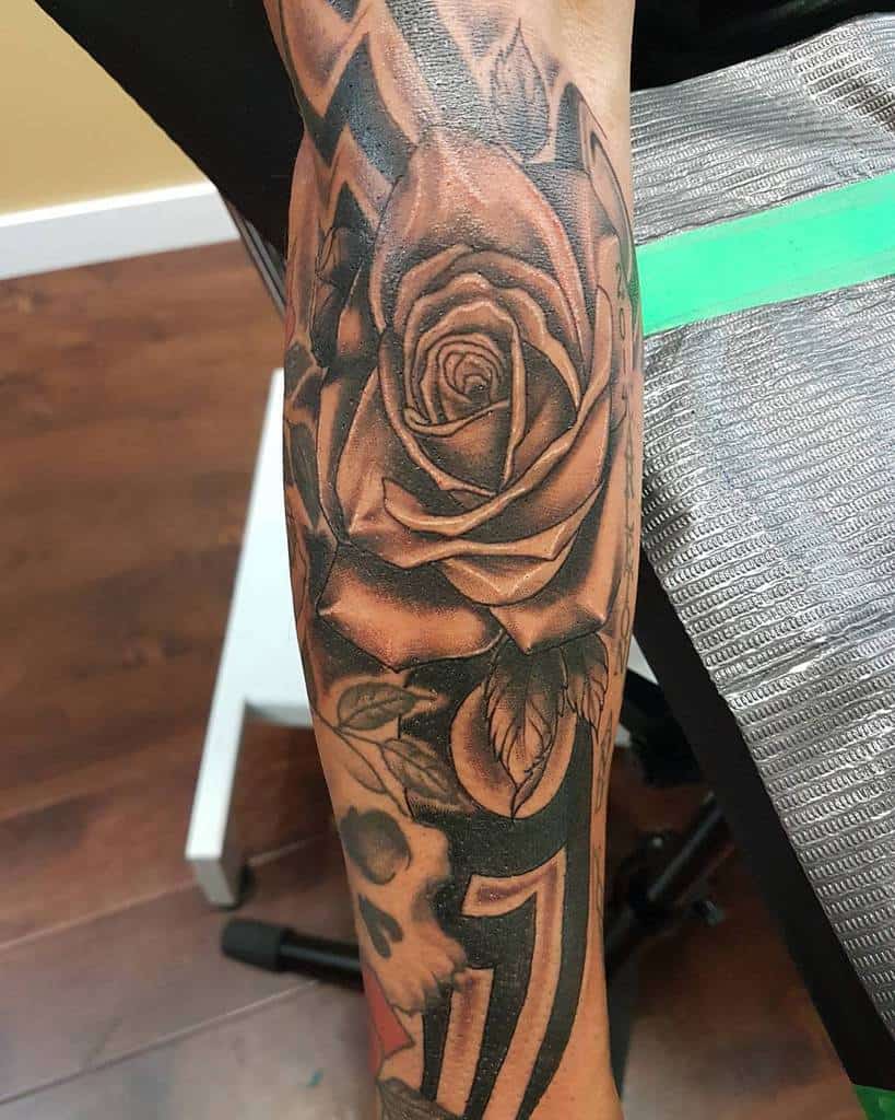 Arm tattoo of a detailed rose with leaves intricately woven into tribal geometric patterns