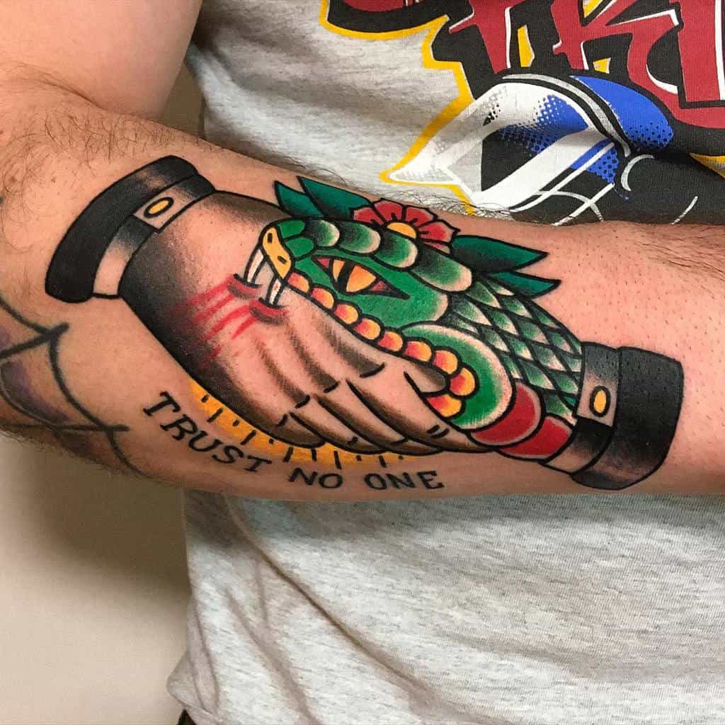 Tattoo of a handshake with a snake wrapped around, text "Trust No One" on forearm