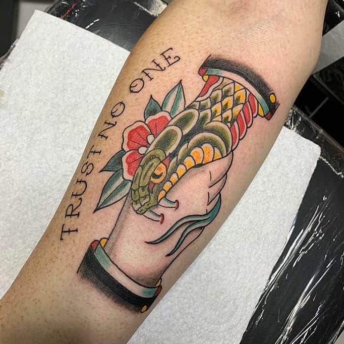 Tattoo of a snake and hand with the words "TRUST NO ONE" on a person's arm