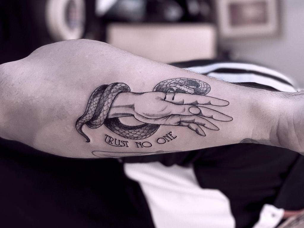 Tattoo of a snake coiled around a hand with the words "Trust No One" on a person's arm