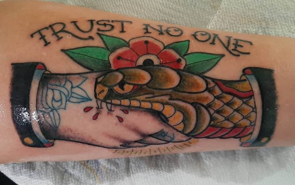 Tattoo of a snake and hand shaking, with "Trust No One" above and a red flower in the background