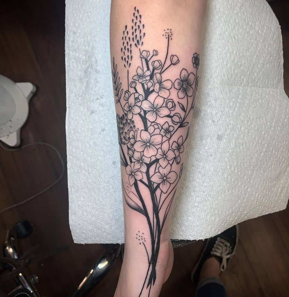 Black ink forearm tattoo of delicate wildflowers and grasses, showcasing fine line details and natural elegance