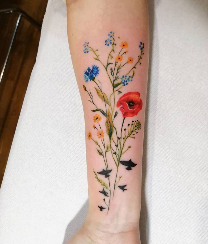 Forearm tattoo of colorful wildflowers and small flying birds